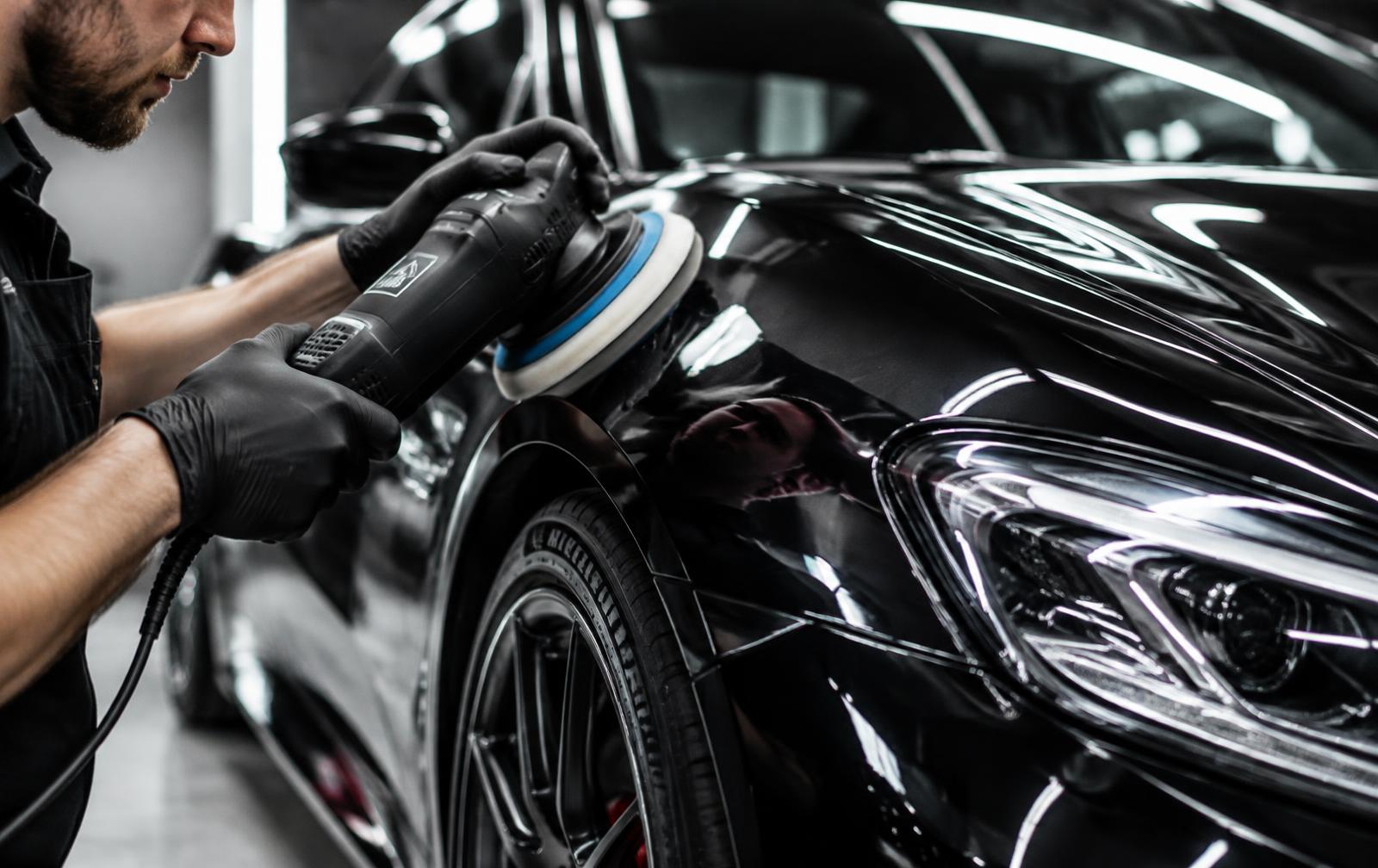 Detailer machine-polishing the paint of a black luxury car